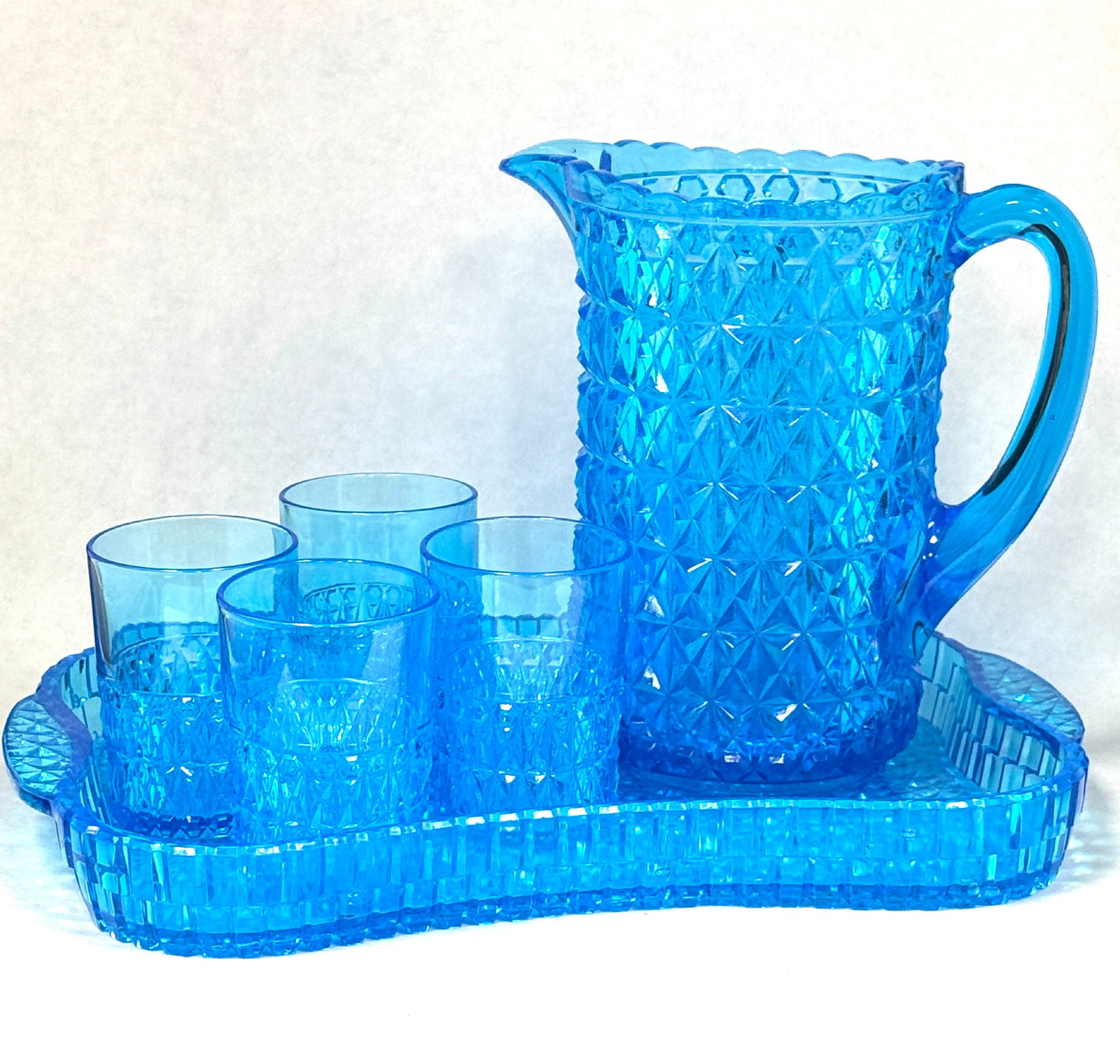 Diamond Point Pitcher- Tumblers: Blue Diamond Point pitcher and 4 tumblers with tray; ht. pitcher 8 1/4". CONDITION: no chips, cracks, repairs, or material defects found, Jaremos attempts to call any material flaw that affects the