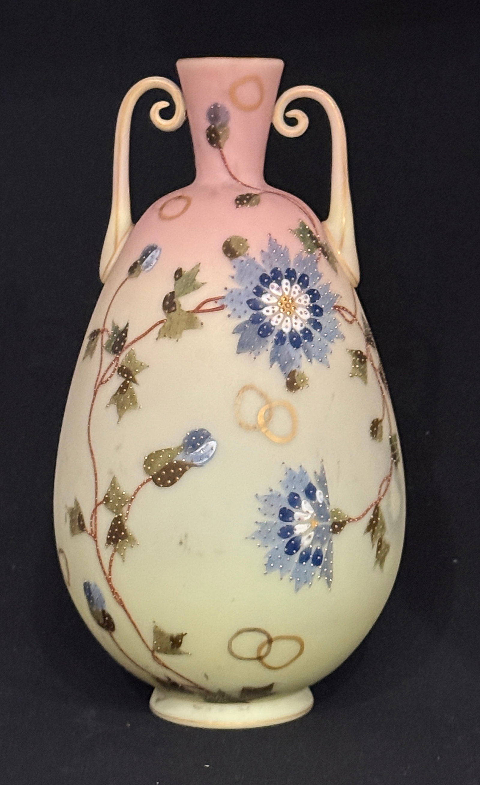 Mt. Washington Two Handle Vase: Mt. Washington two handle Burmese vase, ovoid form with two scrolling Burmese handles decorated with blue and white flowers on green stems and overall gold stippling, 10 1/4" ht. CONDITION: very good