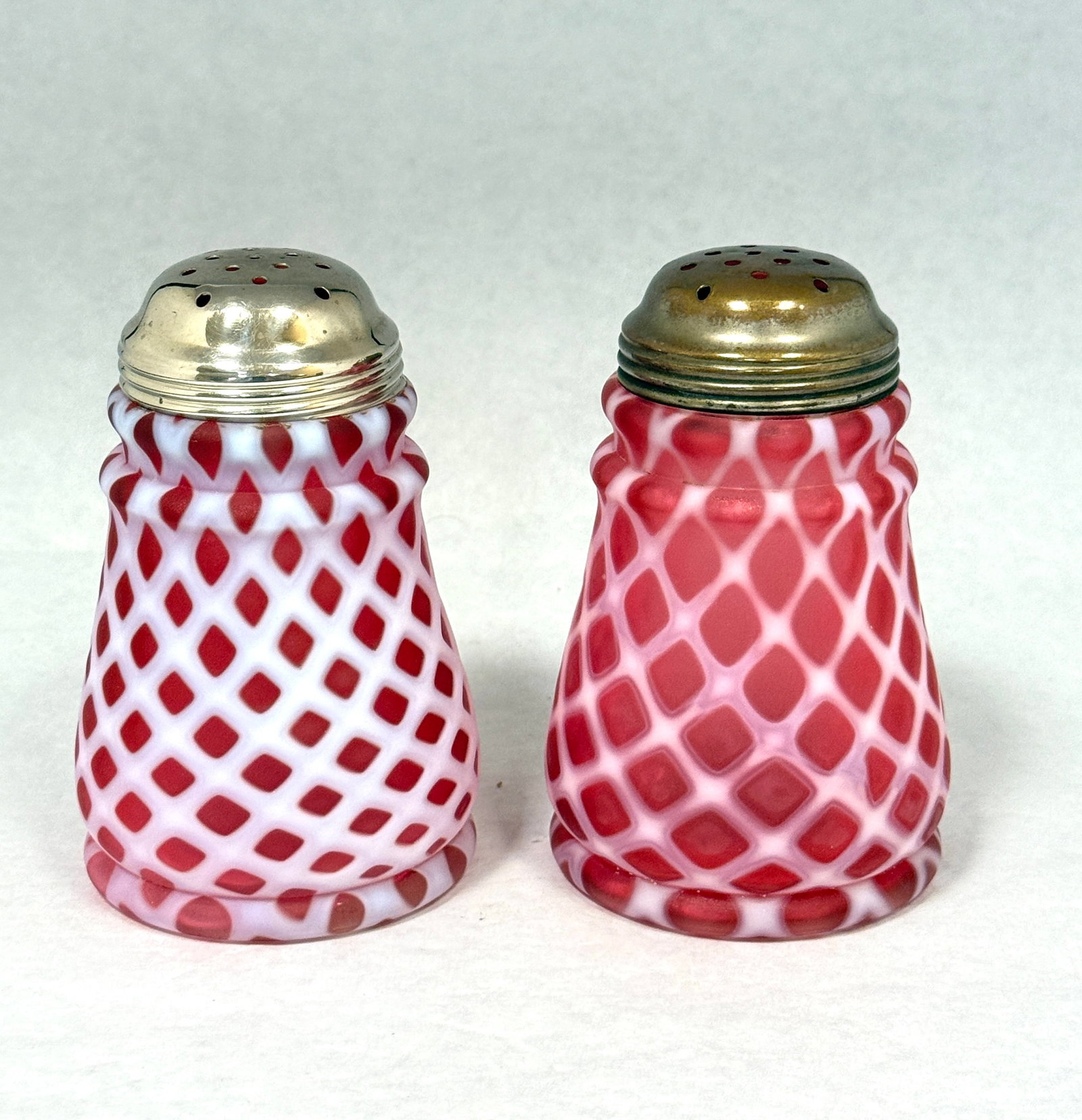 2 Opalescent Lattice Shaker: 2 opalescent tapered lattice sugar shakers in cranberry; ht. 5". CONDITION: no chips, cracks, repairs, or material defects found, Jaremos attempts to call any material flaw that affects the price, but