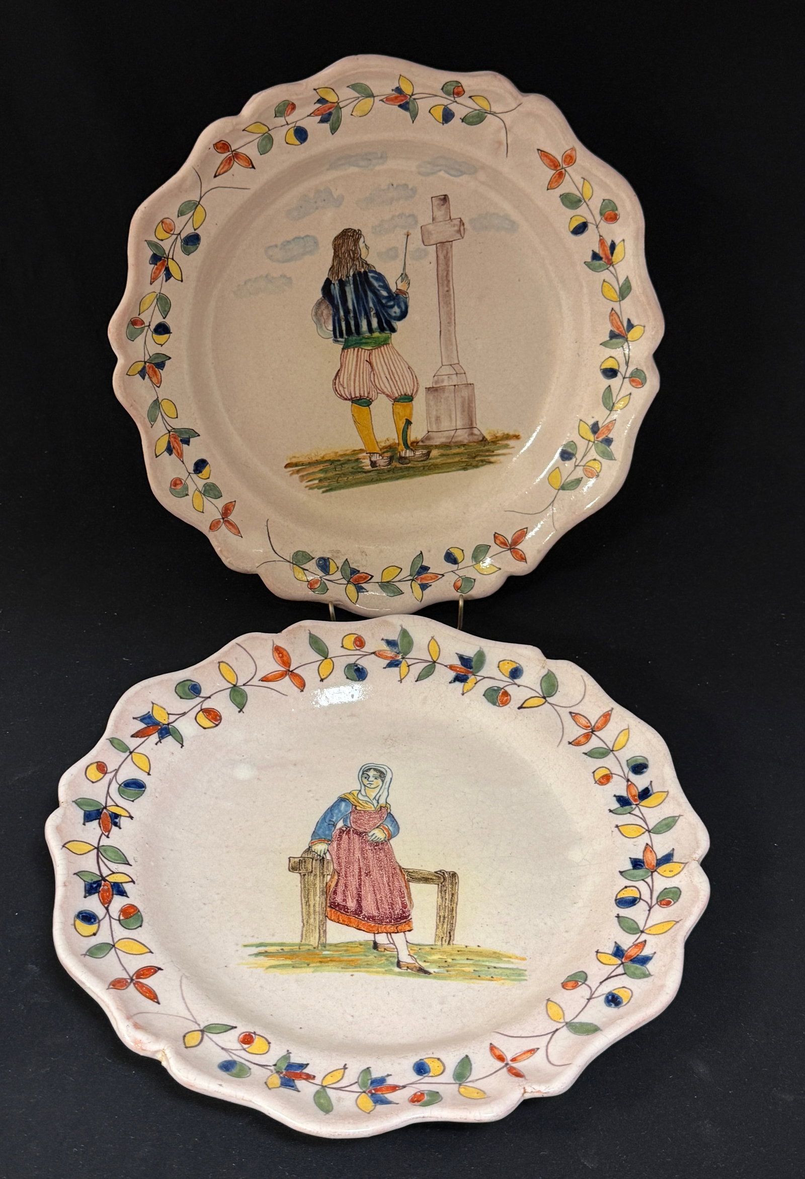 2 Malicorne Plates: 2 Malicorne Faience deep chargers, including Pouplard Beatrix of a Breton in finely painted clothing standing at a cross together with a Bretonne leaning against a railing gazing in the distance,