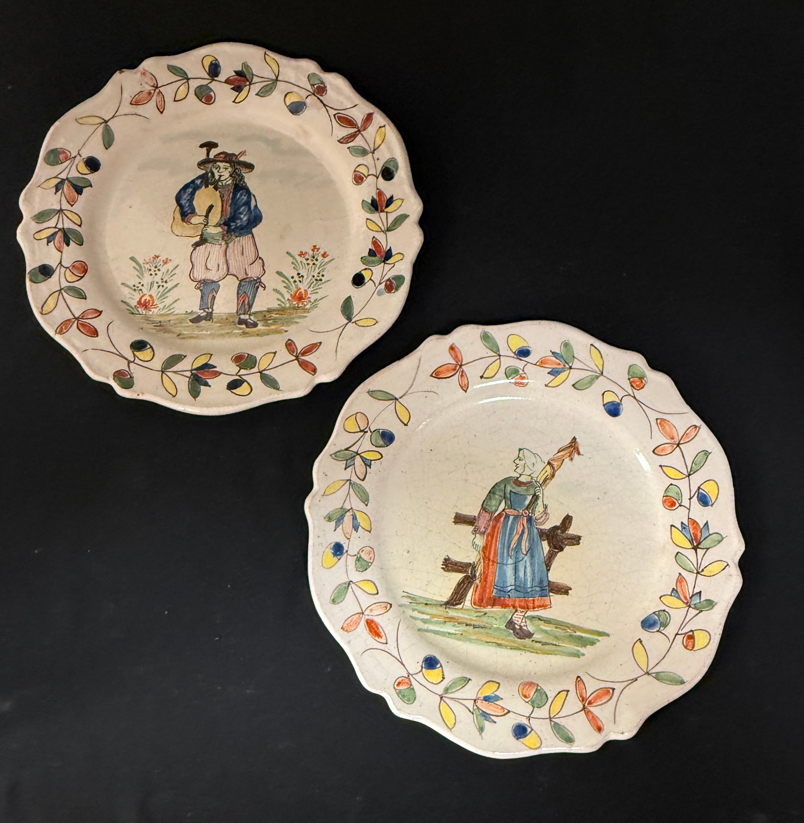 2 Malicorne Plates: 2 Malicorne plates including a Breton playing a biniou together with a Bretonne working with wool, each with a traditional Malicorne border, diameter 9.5" circa 1895-1920. CONDITION: Quimper has