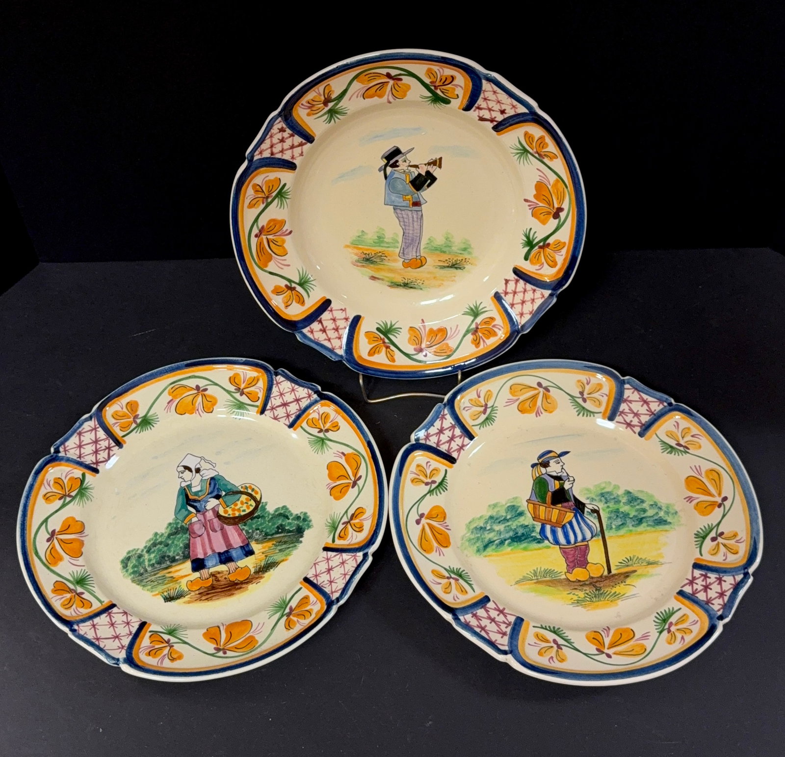3 Pcs HB Quimper: 3 pcs HB Quimper including a shallow bowl and 2 plates decorated with Bretons carrying baskets and one playing a bombarde; diameter 9 1/2" circa 1930-1950. CONDITION: Quimper has propensity to have mi