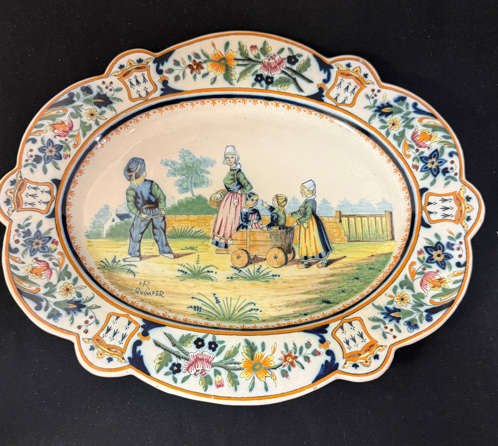 HR Quimper Oval Platter: HR Quimper oval platter with highly decorated border of crests, crowns, ermine tails and floral sprays, scene of a mother and her children heading to market, Breton house seen in background; diameter 