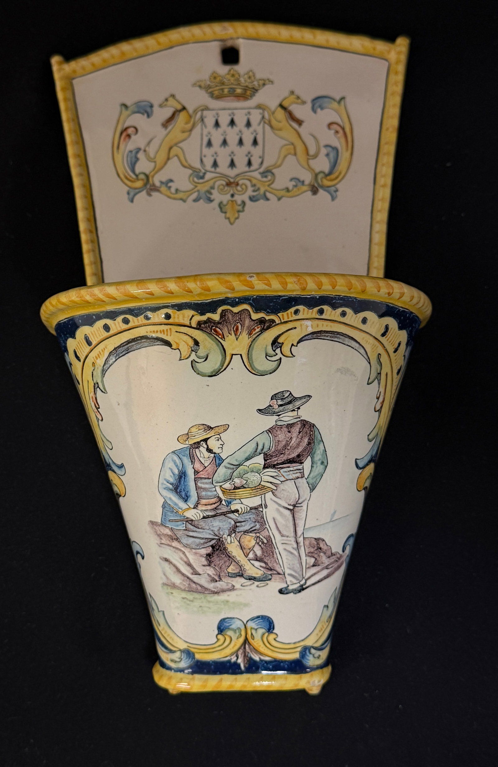 HB Wall Pocket: HB wall pocket with scene of 2 Bretons looking out to sea surrounded by scrolling foliage and topped with the Blason of Brittany; ht. 11 1/4" circa 1883-1904. CONDITION: Quimper has propensity to