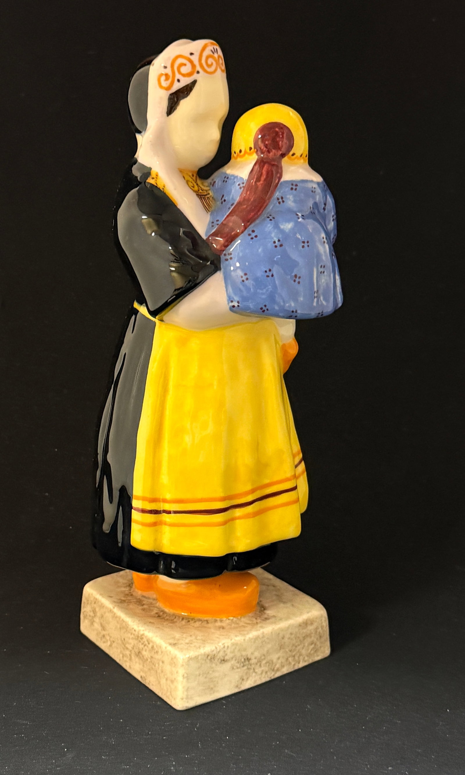 Berthe Savigny Figural: HB Quimper Berthe Savigny young girl and bebe figural, girl wearing clothing with traditional Breton embroidered designs and Celtic designs on her coif, wooden sabots, bebe is wearing a corn flower
