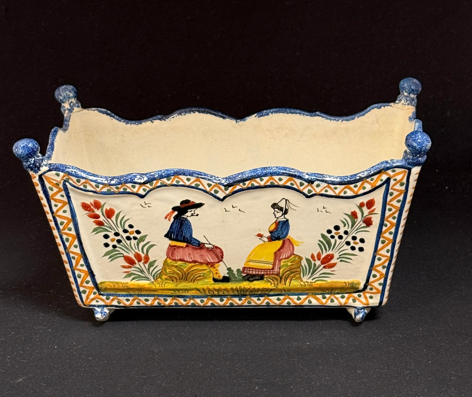 HenRiot Quimper Jardiniere: HenRiot Quimper cradle jardiniere with Breton couple and floral d?cor; length 8 1/2" circa 1920-1950. CONDITION: 3 finials have been reattached. Quimper has propensity to have minor chips, glaze