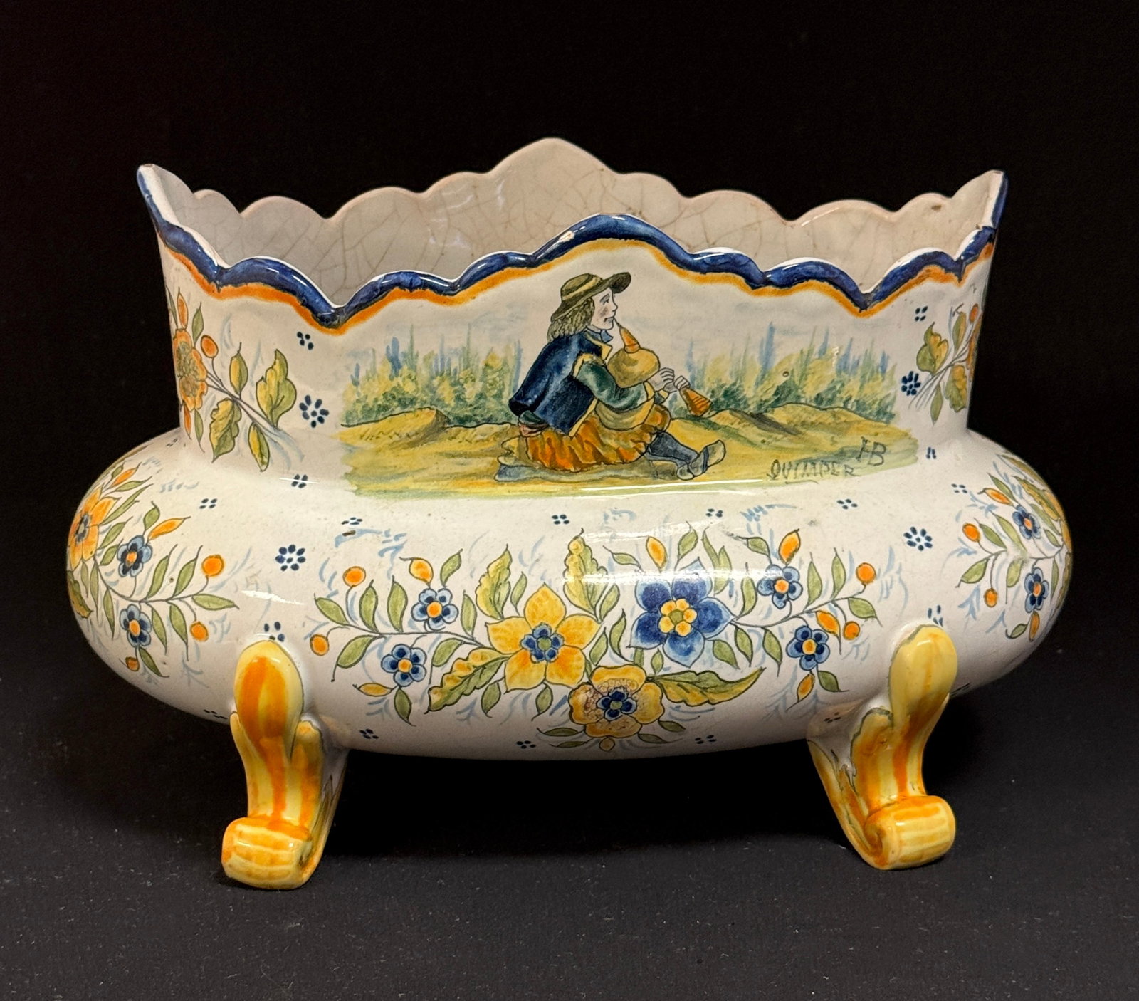 HB Quimper Oval Jardiniere: HB Quimper oval footed jardiniere with shaped rim, a Breton playing a biniou in a woodland scene surrounded by delicate floral sprays; length 10" circa 1904-1940. CONDITION: Quimper has propensity to