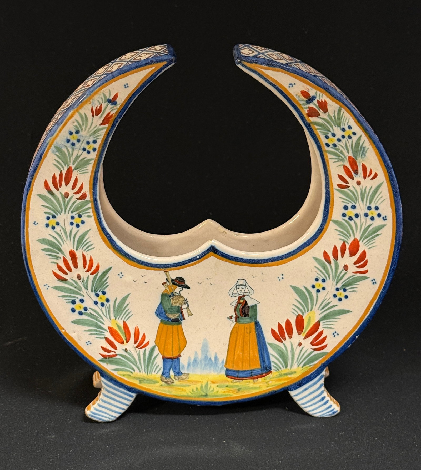 HR Quimper Cresent Jardiniere: HR Quimper crescent shaped footed jardiniere with a Breton couple one playing a biniou on the front, a basket filled with a la touch? foliage and flowers on the back and the sides are intricately