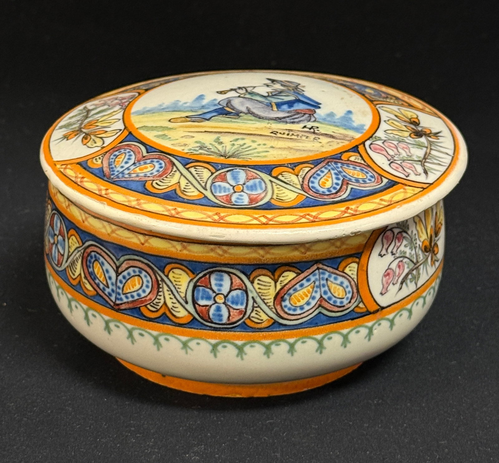 HR Quimper Lidded Bon-Bon: HR Quimper lidded bon-bon with bands of colorful and finely painted Celtic motif, sprigs of ajonc and bruyere surrounding a seated Breton playing a bomarde; diameter 5 1/4" circa 1904-1922. CONDITION: