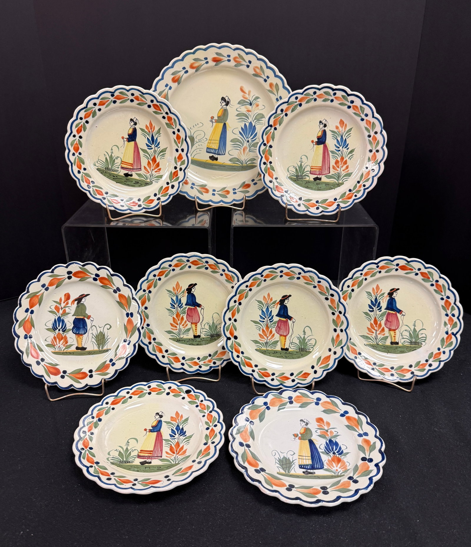 9 HenRiot Quimper Plates: 9 HenRiot Quimper plates one scalloped rim plate with Bretonne together with 8 scalloped smaller plates with Breton figures, all have a la touch? motif on rim; largest 8 3/4" circa mid 20th century.