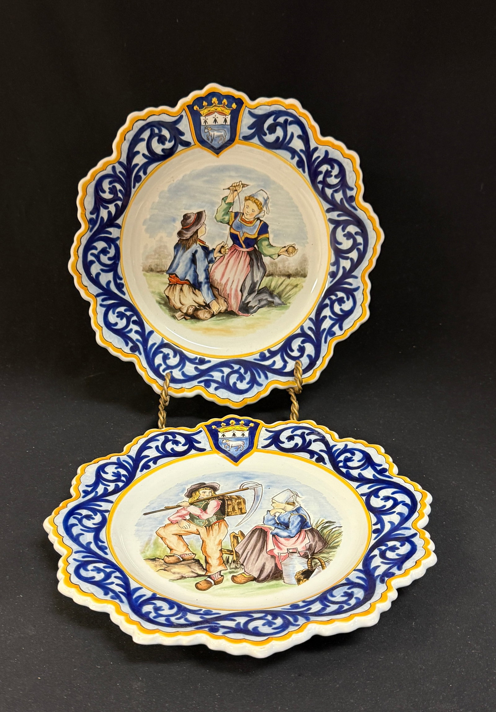 PR HenRiot Quimper Plates: 2 PR HenRiot Quimper Plates with decor riche and Blasons of Quimper topping the border, one plate has Breton couple at rest between farm chores, the other a Breonne working wool with help of a