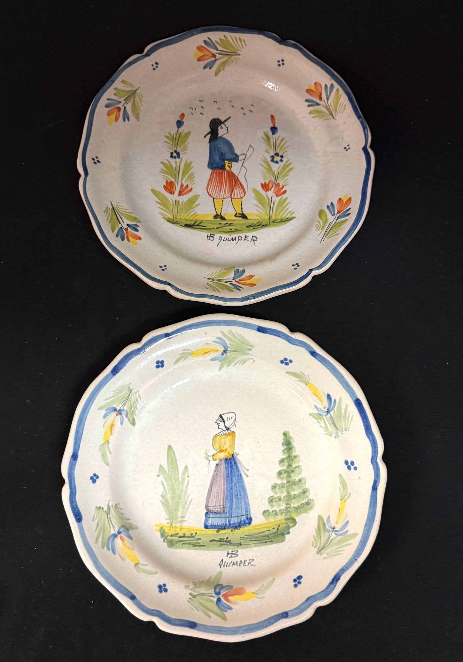 2 HB Quimper Plates: 2 HB Quimper plates with Breton figures, 4 dot and a la touch? border motifs and Bretons flanked with floral sprays; diameter 9 1/4" circa 1920 -1940. CONDITION: loss to rim on back of one plate.