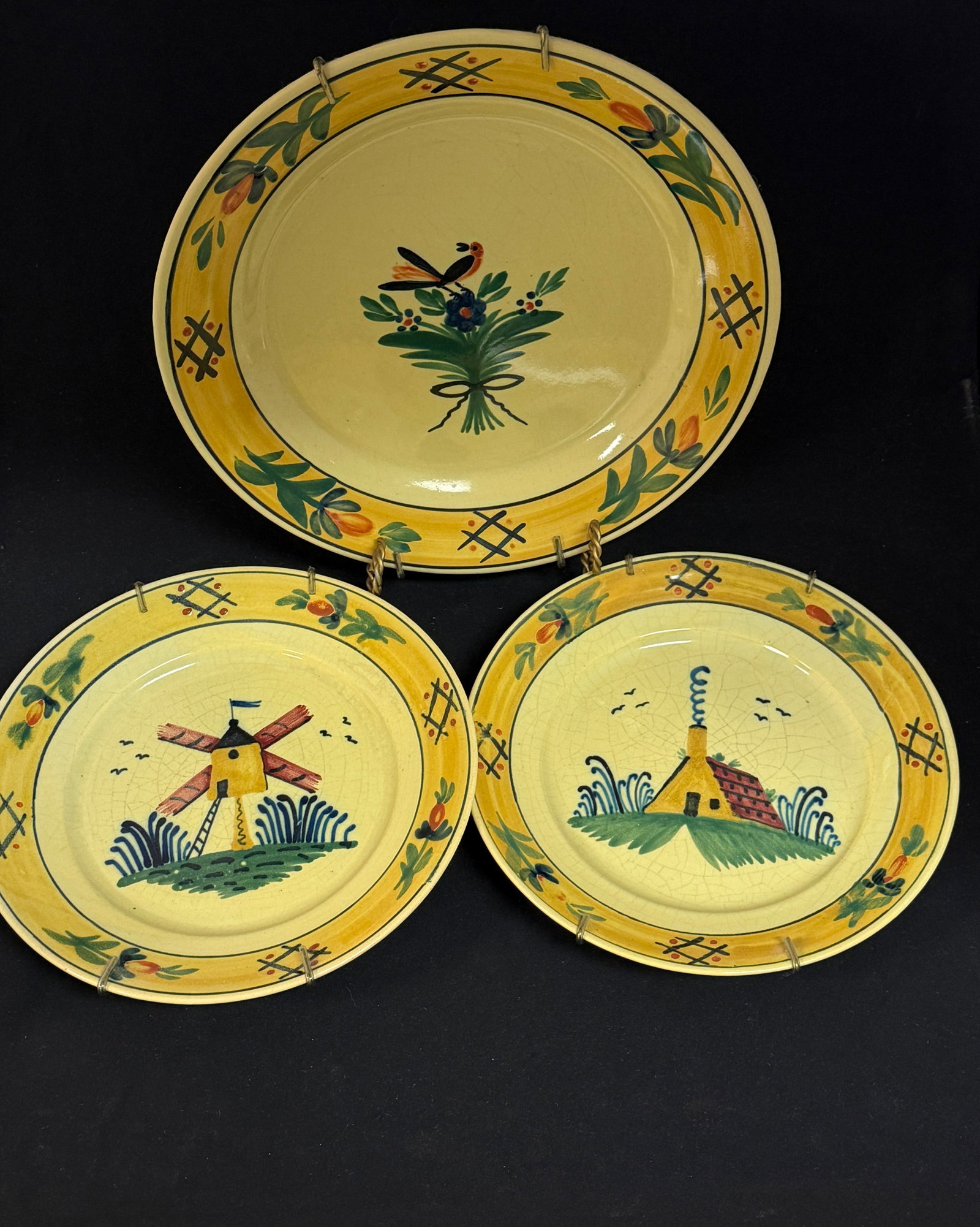 3 HB Quimper Items: 2 HB Quimper Soleil deep plates with windmill, cottage, and smoke rising from chimney with a large deep plate with a bird atop a bouquet of flower; largest diameter 11 3/4" circa 1920-1940.