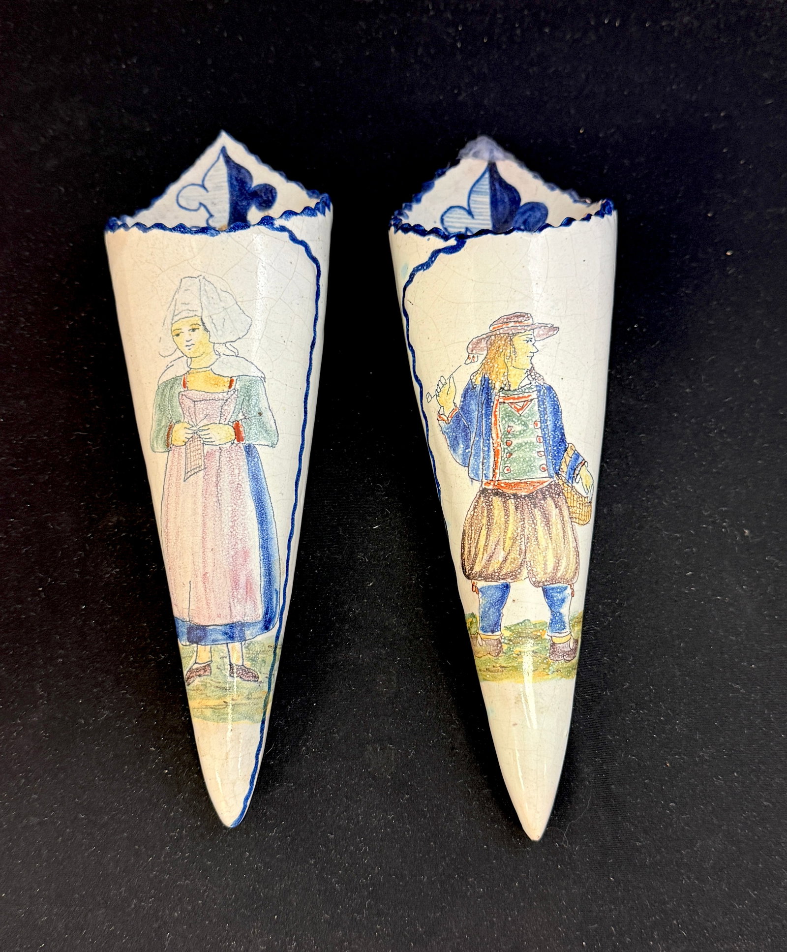 Pair Malicorne Wall Pockets: Pair Malicorne cornet form wall pockets with Breton couple in soft colors, Breton carrying a pipe and basket, Bretonne holding a handkerchief; length 10 3/4" circa 1895-1920. CONDITION: restoration to