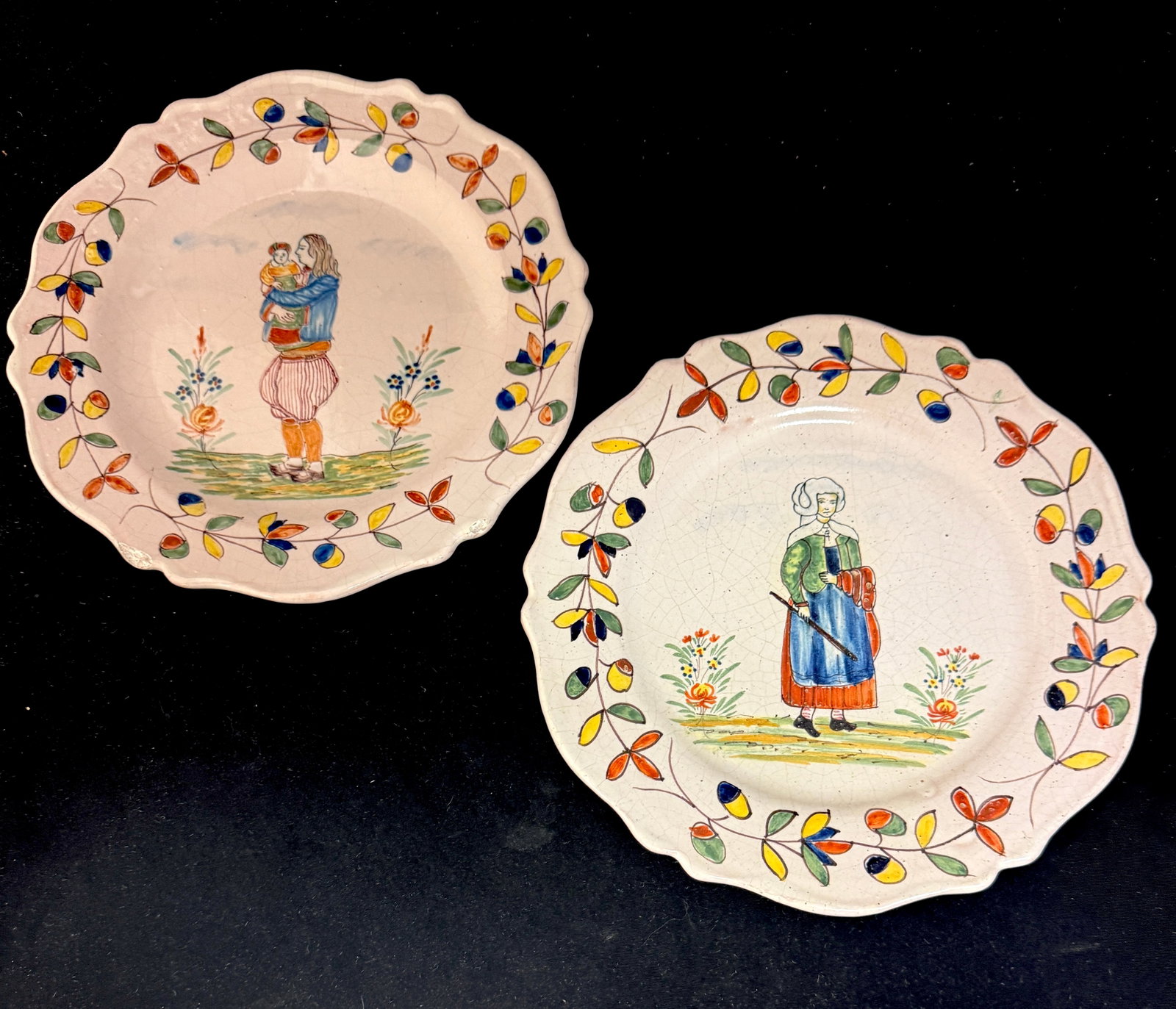2 Malicorne Plates: 2 Malicorne plates, one with Breton father holding baby, the other a Bretonne with walking stick, both have traditional Malicorne border; diameter 9 3/4" circa 1985-1920. CONDITION: chips on front of