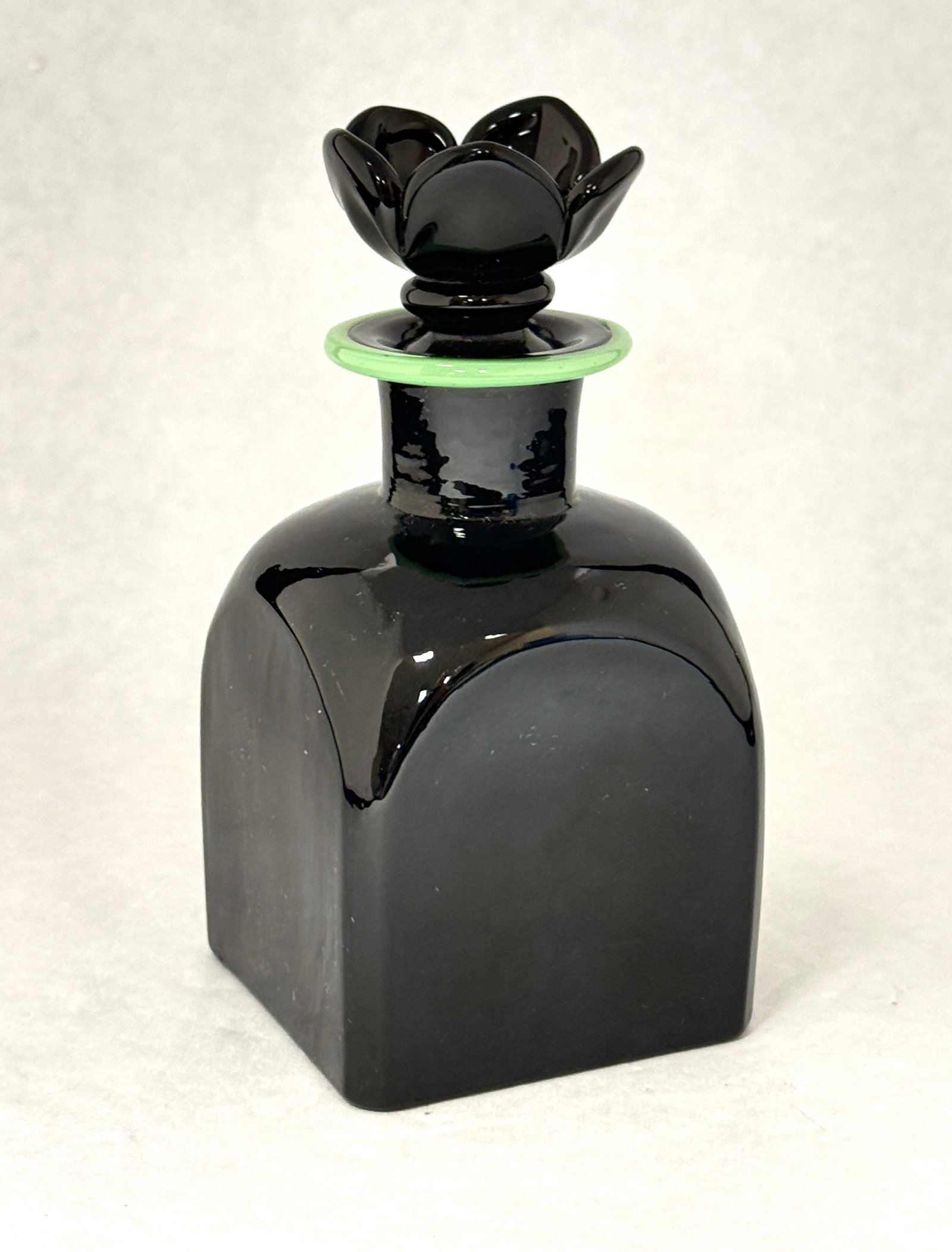 Steuben Black Bath Bottle: Steuben Mirror Black bath bottle with a green lip wrap and a flower stopper, signed with a Fleur de Lis, 5 1/4" ht. CONDITION: no chips, cracks, repairs, or material defects found, Jaremos attempts