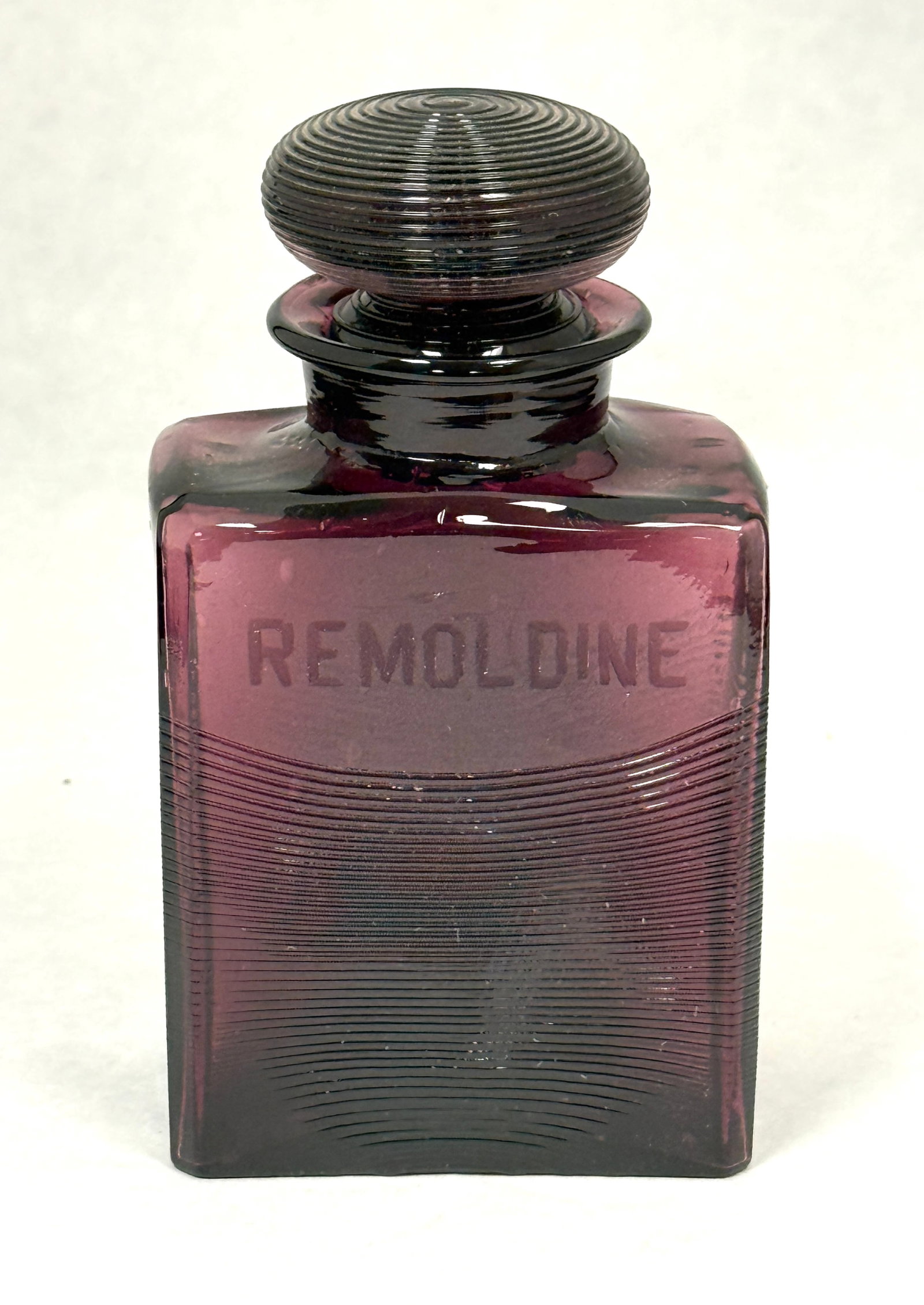 Steuben Purple Bath Bottle: Steuben rectangular form purple bath bottle with controlled threading and block letters "REMOLDINE", 5 1/4" ht. CONDITION: no chips, cracks, repairs, or material defects found, Jaremos attempts to