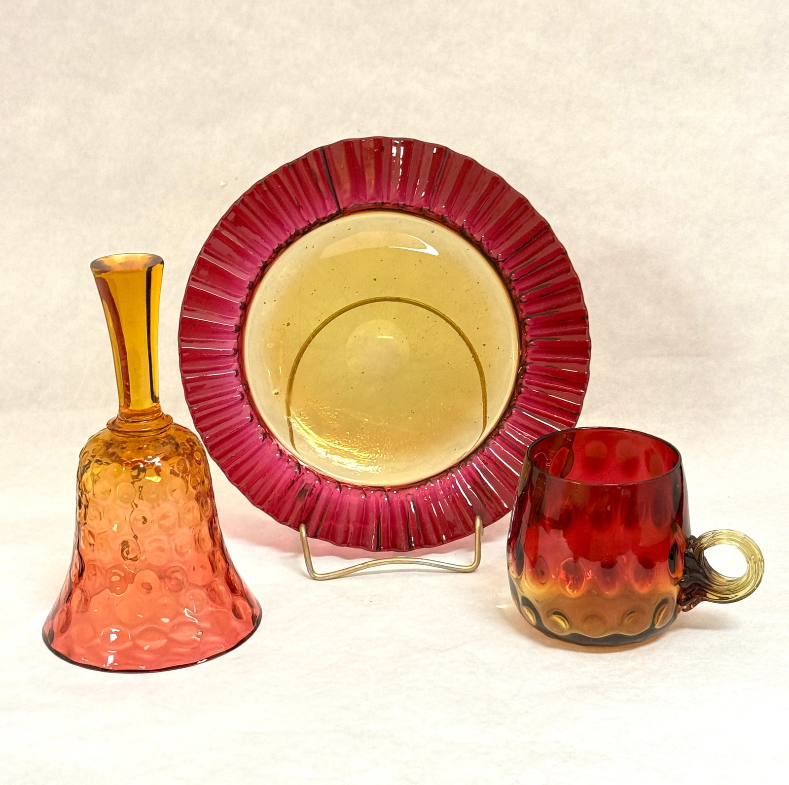 Three Amberina Glass Items: Three Amberina Glass items including a bell, a mug and a plate: bell 6" ht. CONDITION: no chips, cracks, repairs or material defects found, Jaremos attempts to call any material flaw that affects the