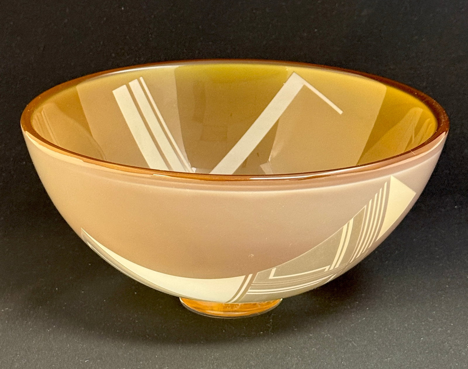 Klas Goran Tinback Amber Bowl: Kosta Boda art glass bowl in amber with a geometric cameo design set on a clear foot, signed K G Tinback 1982, 9 1/2" wide. CONDITION: no chips, cracks, repairs, or material defects found, Jaremos att