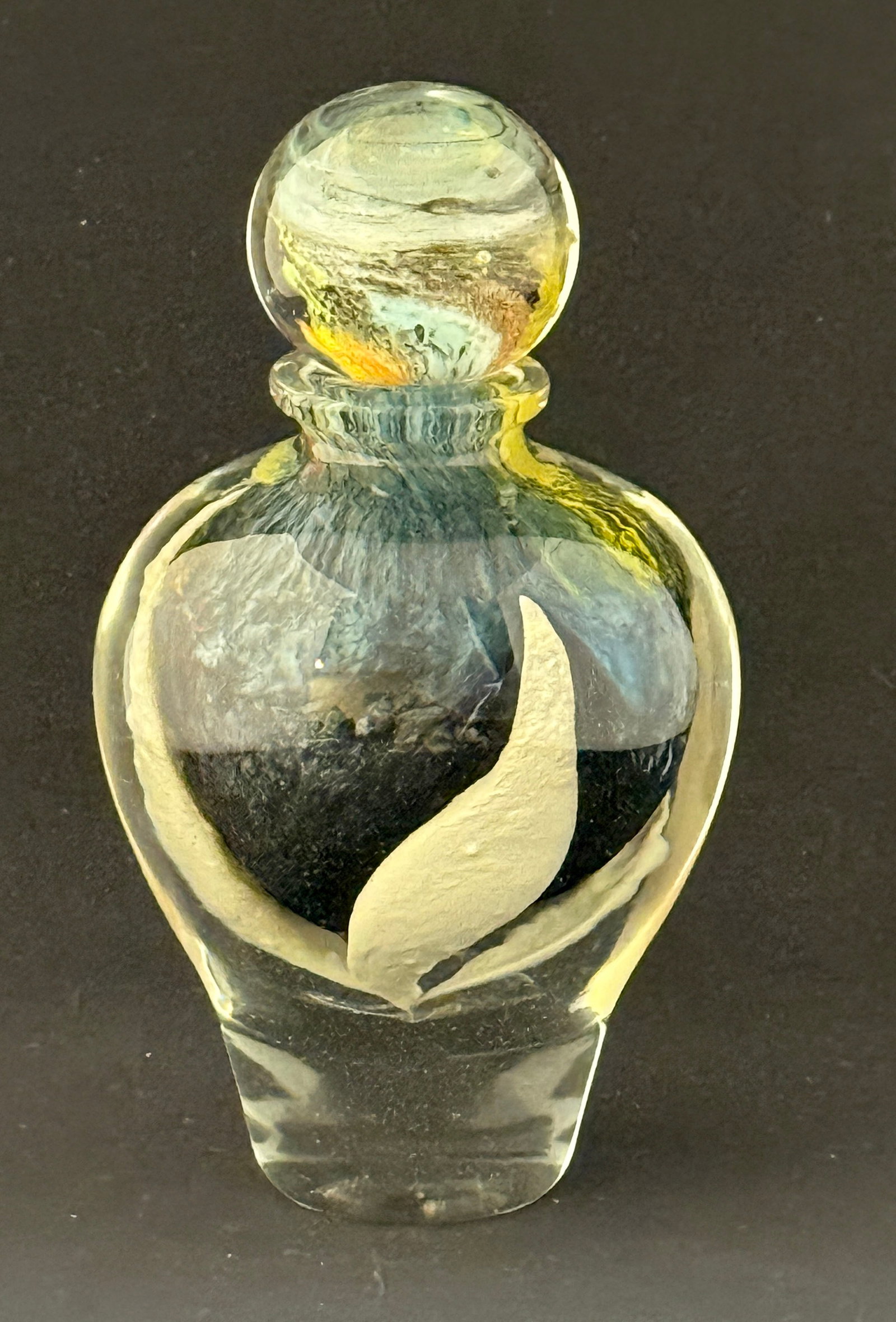 Novaro Art Glass Perfume Bottle: Jean Claude Novaro small clear with blue and white core perfume bottle with ball shaped dobber with green, yellow and blue swirling colors, signed JC Novaro '98; ht. 8". CONDITION: no chips, cracks,