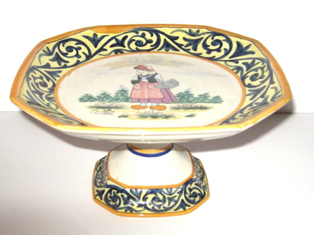 HB Quimper cake stand with Bretonne,: wearing coif and sabots, holding a basket decorated with blue and yellow dŽcor riche border. Approx. 8" dia. c.1930.