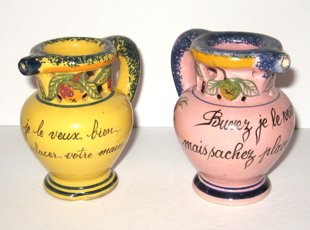 Rare colors - (2) Malicorne puzzle jugs,: pink and yellow ground with French phrase translating: Drink as I would very much like, know where to place your hand. 4" ht. Both marked Henriot Quimper, c.1930-1940.