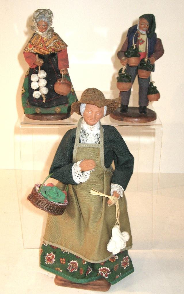 (3) Santons from Provence on terracotta bases: and dresses in country attire including (1) woman with string of garlic, (1) woman with a basket and (1) man carrying pottery jugs. Marked "Santons Jolande France" and "M Chave Aubagne" Tallest 10"H.