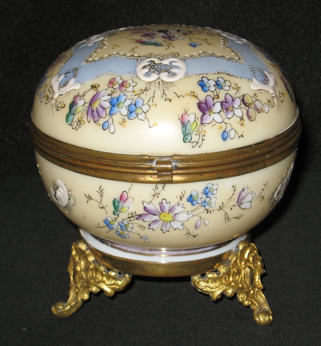 Decorated opaline dresser box,: ovoid form on scrolling metal feet in cream colored glass decorated with blue ribbons and clusters of flowers, 4 1/2" wide.