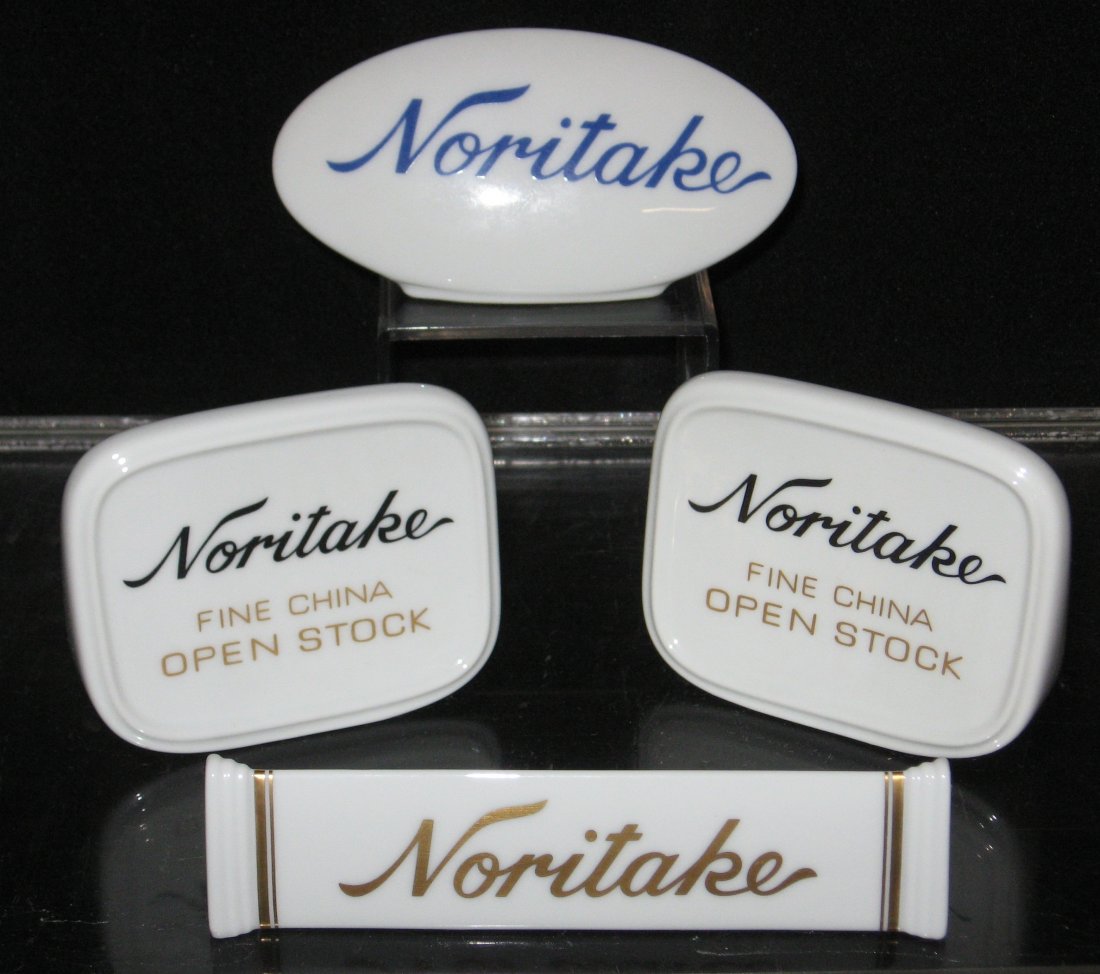 Four porcelain Noritake retail signs,: including one elongated with gold lettering front and back, two rectangular with blue and gold writing front and back and a footed oval, longest 5 3/4" wide.