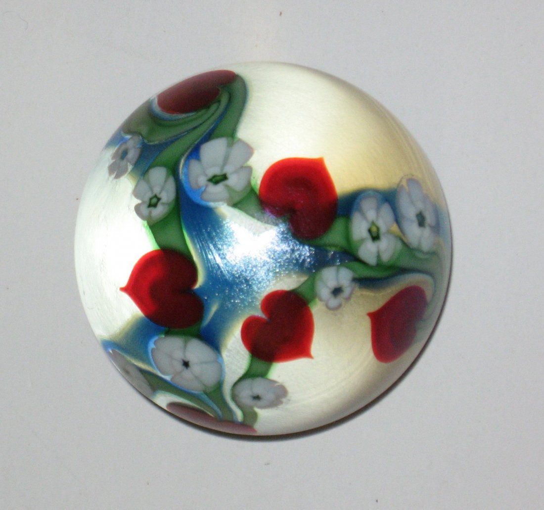 Orient and Flume glass paperweight,: Frosted glass with a blue iridescent ribbon decorated with red heart and white Millefiori on green stems, signed Orient and Flume 1985, 2 1/4" wide.