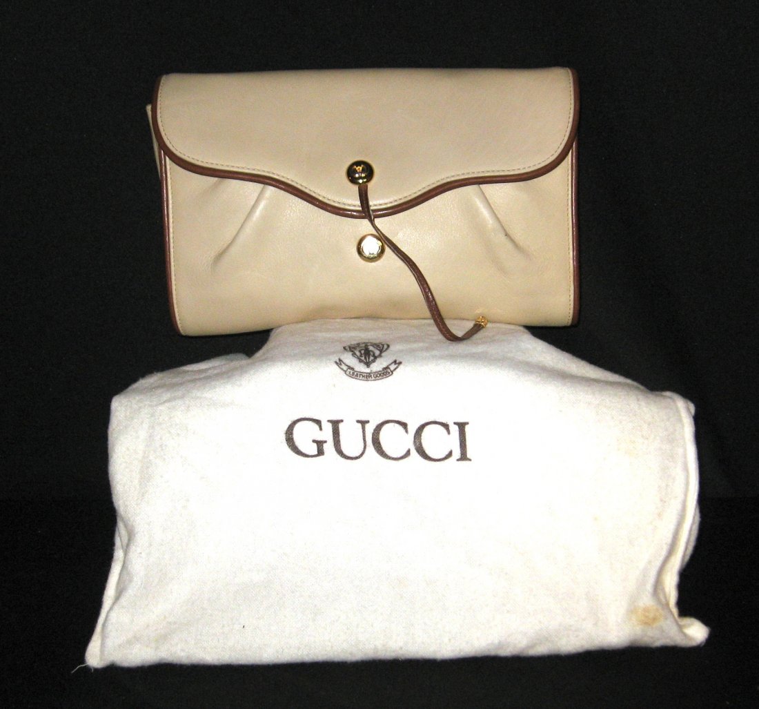 Gucci beige leather clutch,: cream colored bag with brown trim and a brown carrying strap, gold hardware marked Gucci made in Italy has imports and inspection tags, cloth bag marked Gucci, 9 1/2" long by 6" ht.
