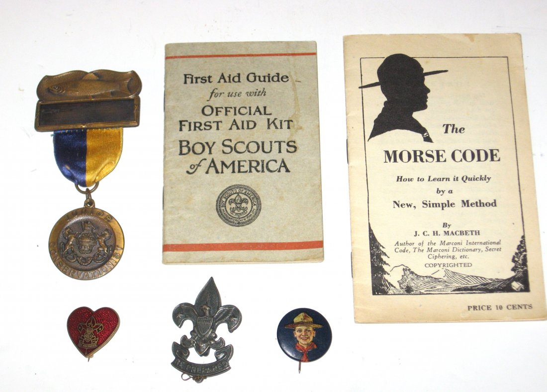 Three Vintage 1920 Boy scout pins,: Including a Heart pin, Junior Conservationist, a 1911 eagle pin and a Celluloid metal pin with pictorial of a scout. Together with a 1922 Morse Code booklet and a 1932 First aid booklet.