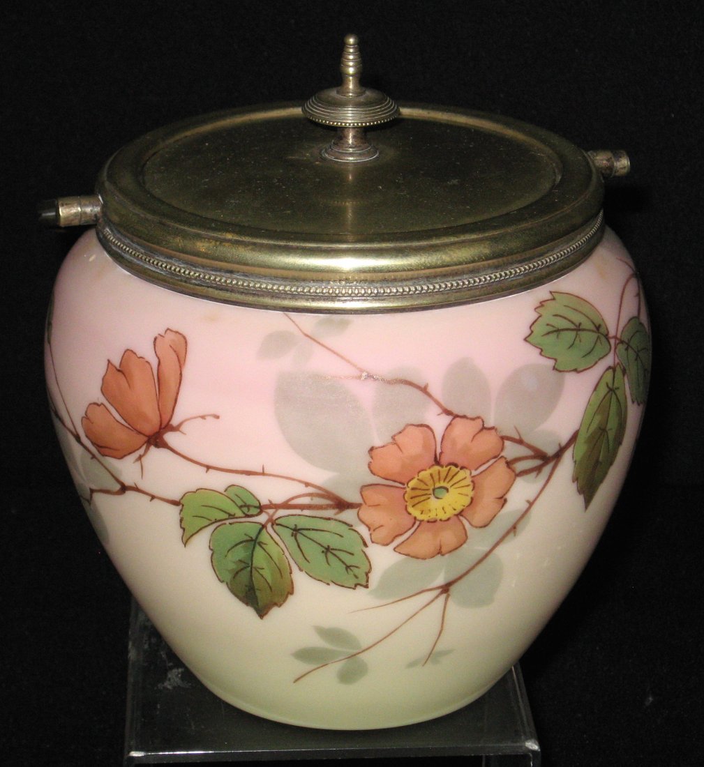 Webb Burmese biscuit jar,: Ovoid form in amber shading to salmon decorated with large red Primrose on green leafy stems, metal handle with unique ball adornment, 9 1/2" ht.
