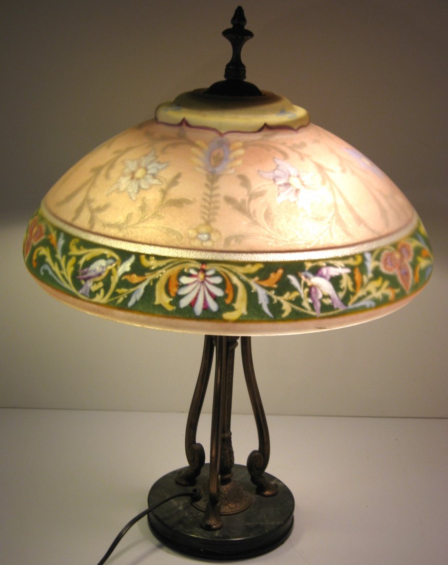 Pairpoint reverse painted lamp,: Pink shade with a green border decorated with random flowers and scrolling, set on a three arm bronze base with marble bottom, shade marked The Pairpoint Co. 16" wide, three arm base 22" ht.