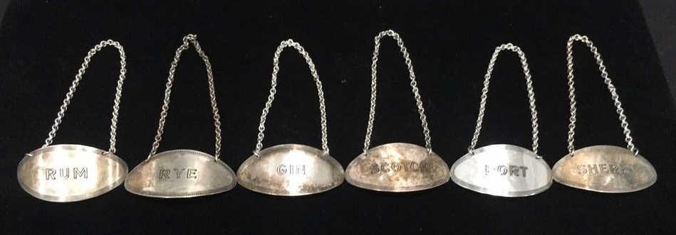 Six liquor bottle labels: Silver plate, 2 inches wide