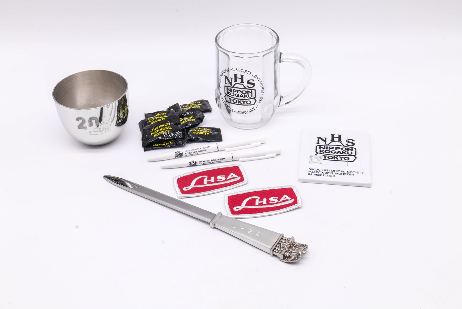 LHSA and NHS Promotional Items: LHSA and NHS promotional items, made for the Leica Historical Society of America and the Nikon Historical Society. Included are cloth patches, NHS pens, candy, coffee mug, letter game, letter opener a