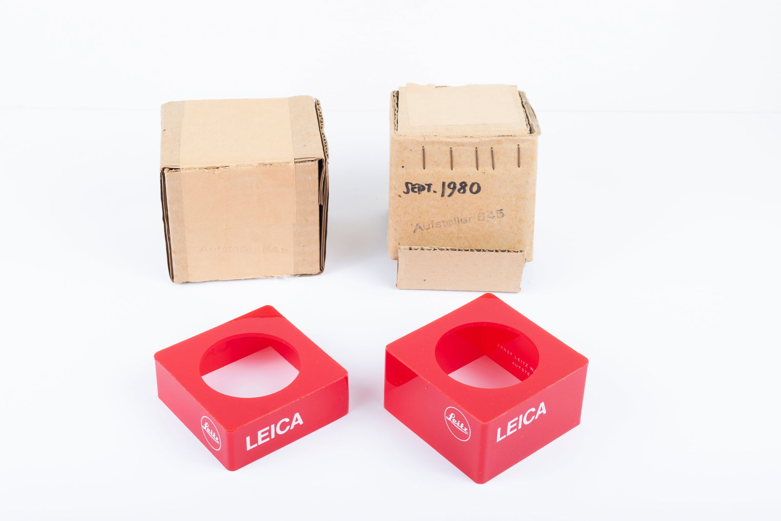 Two sets of red plastic lens display stands: Two sets of red plastic lens display stands, marked “Leica” and “Leitz,” in two sizes, in their original boxes, which are marked “Aufsteller 645.”Condition: Mint overall