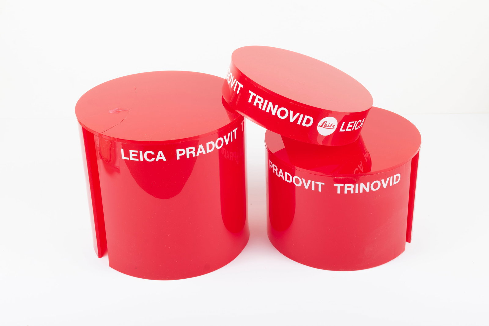 Three nesting red plastic display columns: Three nesting red plastic display columns, marked “Leica Pradovit Trinovid” and “Leitz.” The largest column has a crack and has been repaired. Otherwise, these are like new and in