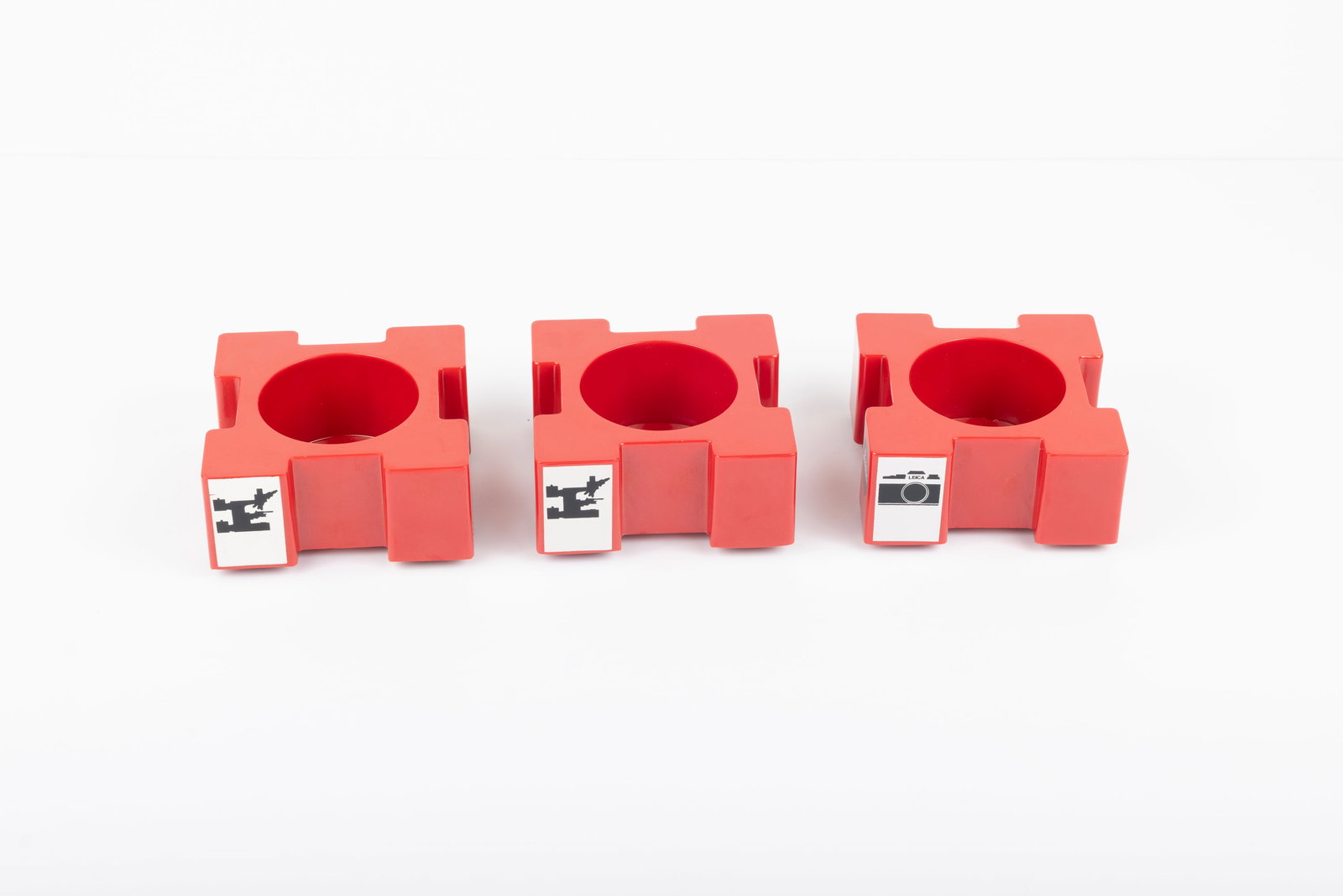 Three Leitz red plastic lens display stands: Three Leitz red plastic lens display stands. One shows a camera, and the other two show a microscope.Condition: Near Mint
