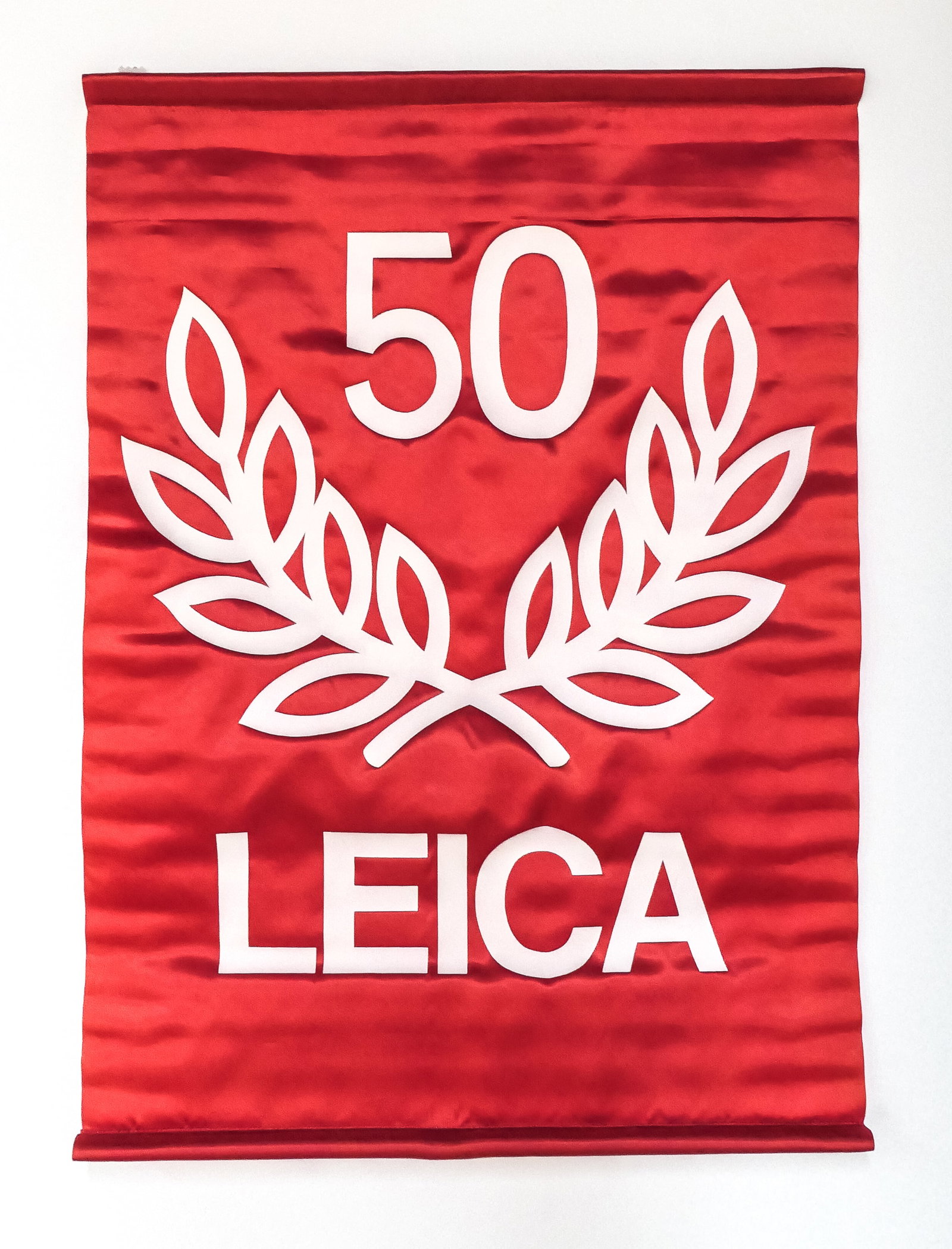 Leica "50 Year" satin banner: Leica “50 Year” satin banner, made in 1975 for the 50th Anniversary of the Leica camera. Made by Hollywood Banners in New York, this wall hanging banner measures approximately 31" tall by 22"