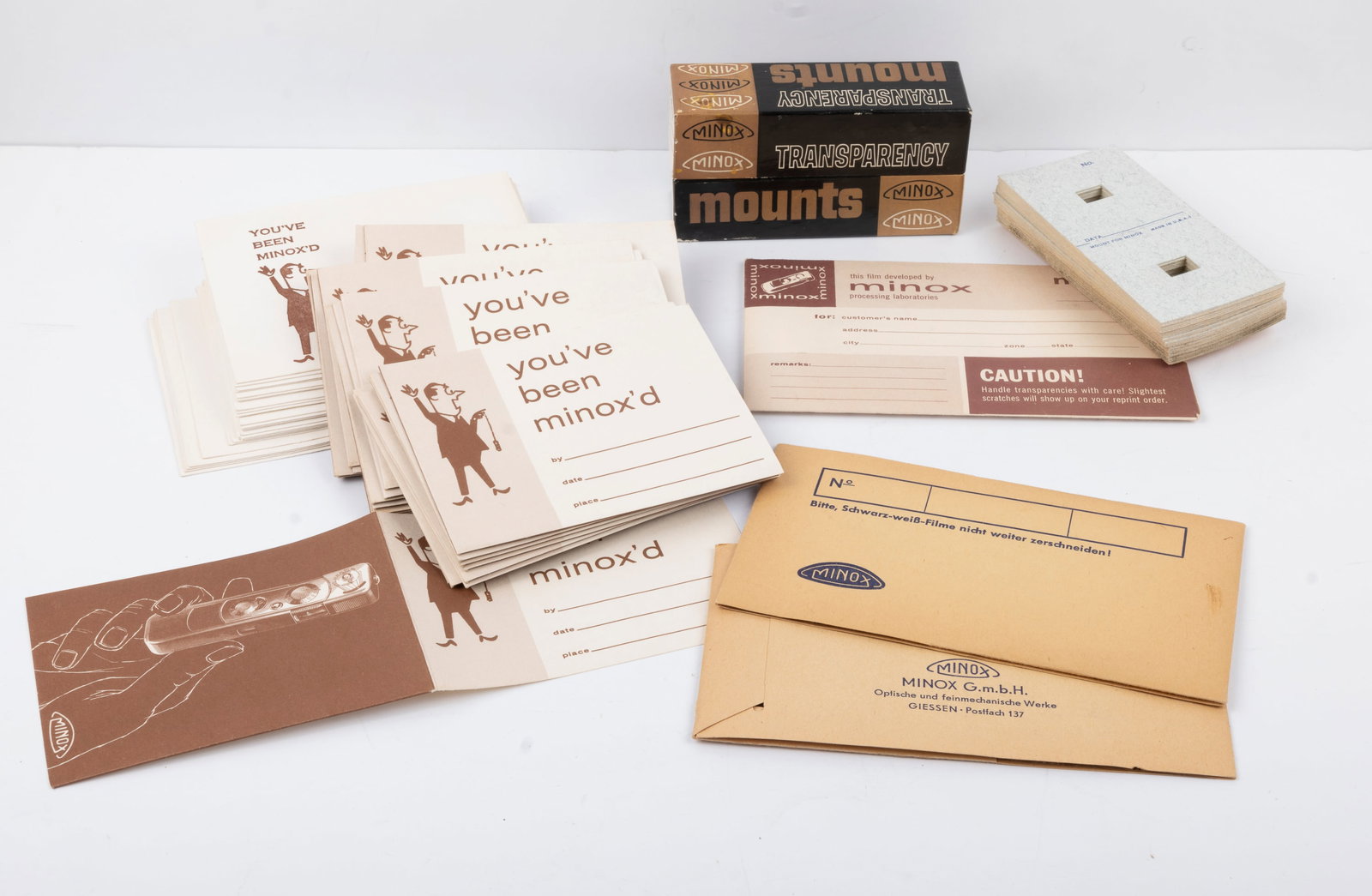 An array of Minox films: An array of Minox films and transparency accessories, including a box of transparency mounts, blank slide masks, three plastic negative sleeves, and “You've Been Minoxed” presentation folders