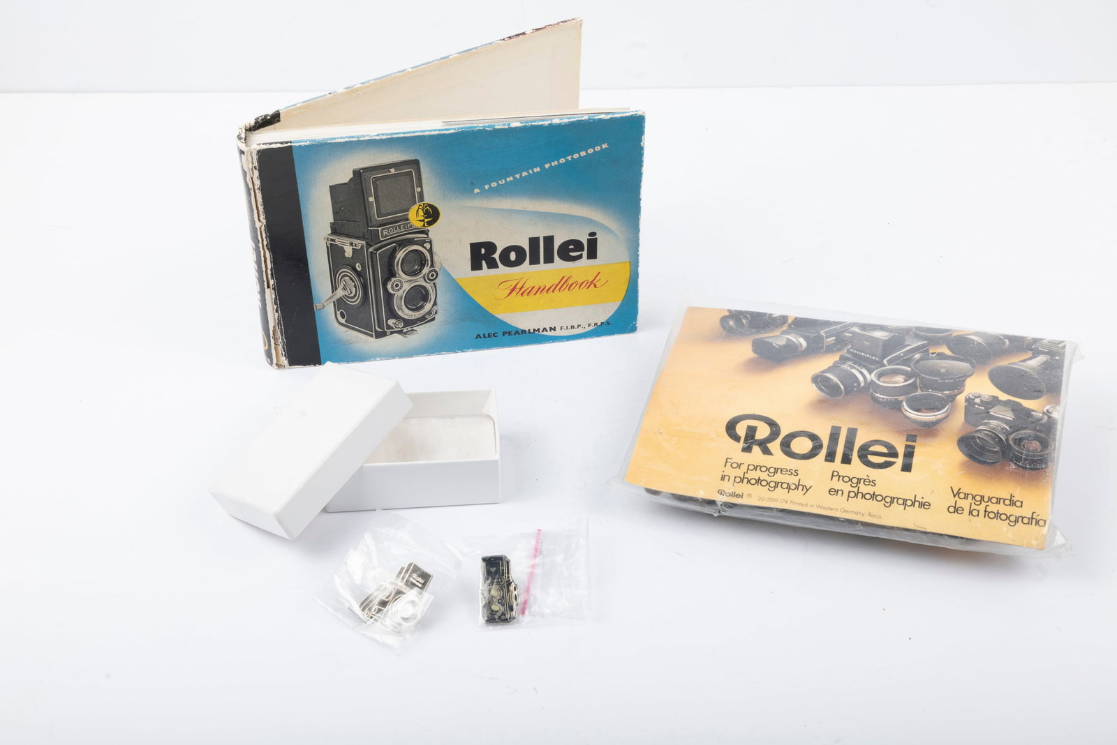 The Rollei Handbook: The Rollei Handbook, “Rollei For Progress in Photography” jigsaw puzzle, and a pair of Rollei enamel pins.Condition: Near Mint