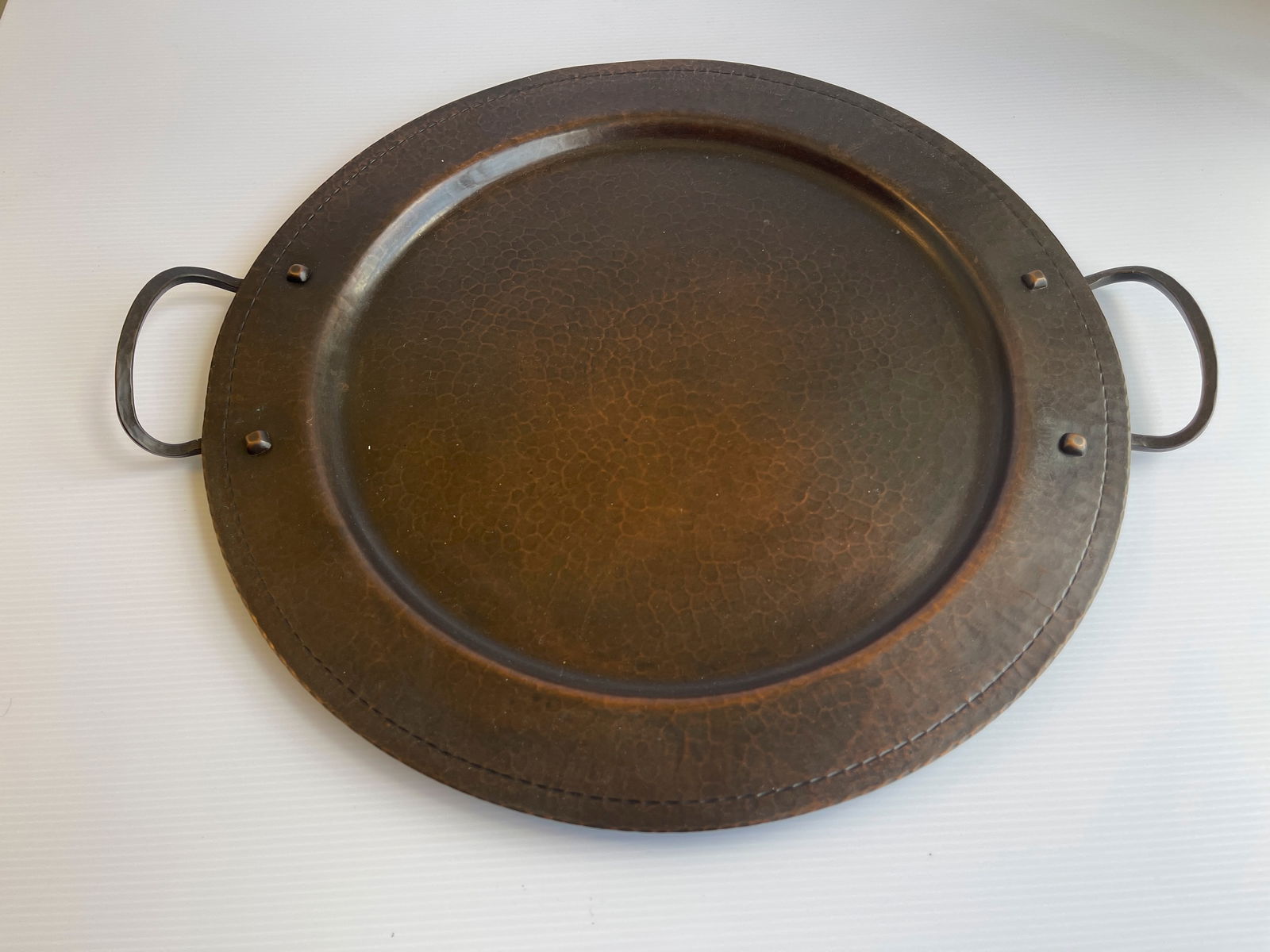 ROYCROFT HAMMERED COPPER TWO-HANDLED SERVING TRAY: ROYCROFT HAMMERED COPPER TWO-HANDLED SERVING TRAY. CIRCA 1915. 16 INCHES AROUND. 18 INCHES WIDEST AT HANDLES