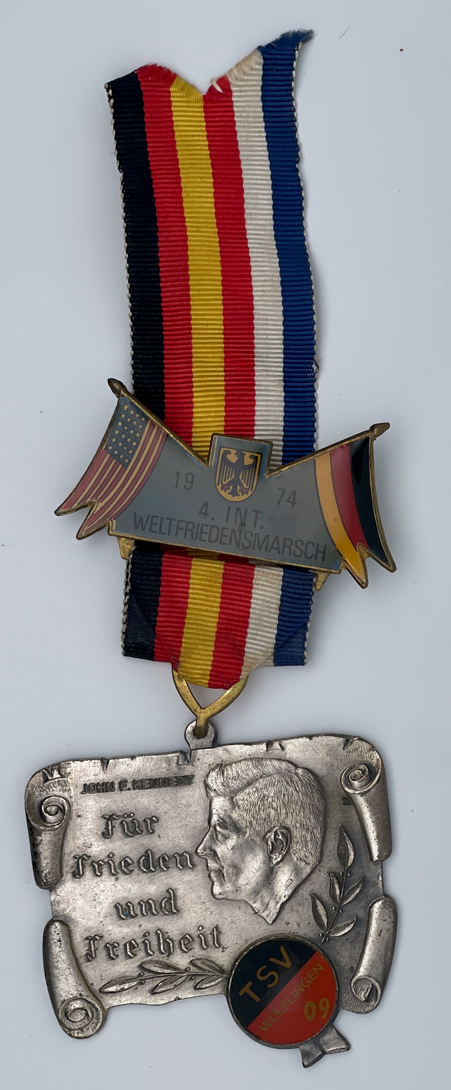1974 John F. Kennedy World Peace March Medal: The image shows a 1974 John F. Kennedy World Peace March Medal. This medal commemorates the 4th International World Peace March and features a portrait of John F. Kennedy, along with the American and 