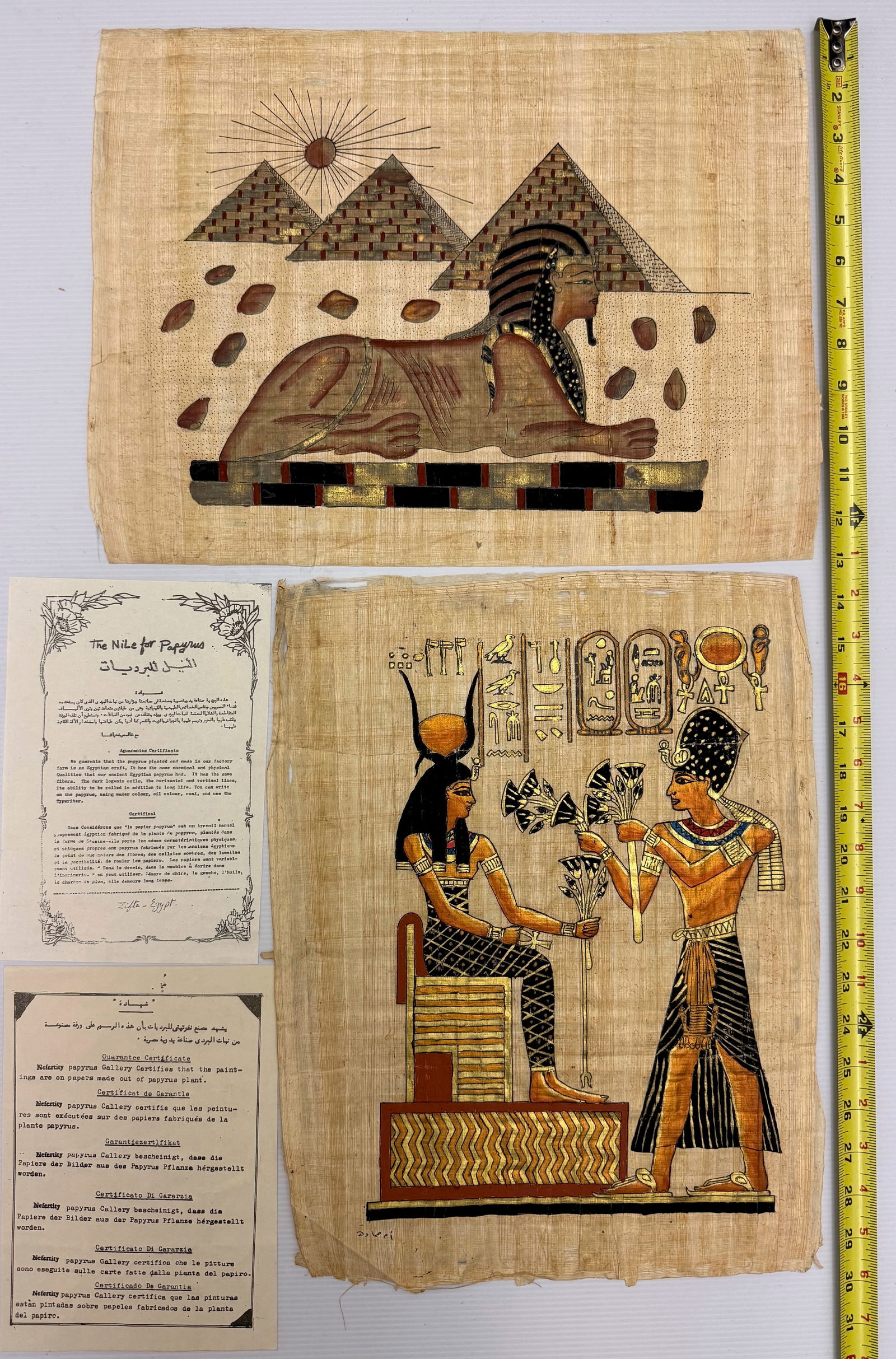 hand-painted Egyptian papyrus artworks: The image shows two hand-painted Egyptian papyrus artworks, along with accompanying authenticity certificates. These pieces typically depict traditional Egyptian motifs, such as the Sphinx, pyramids,