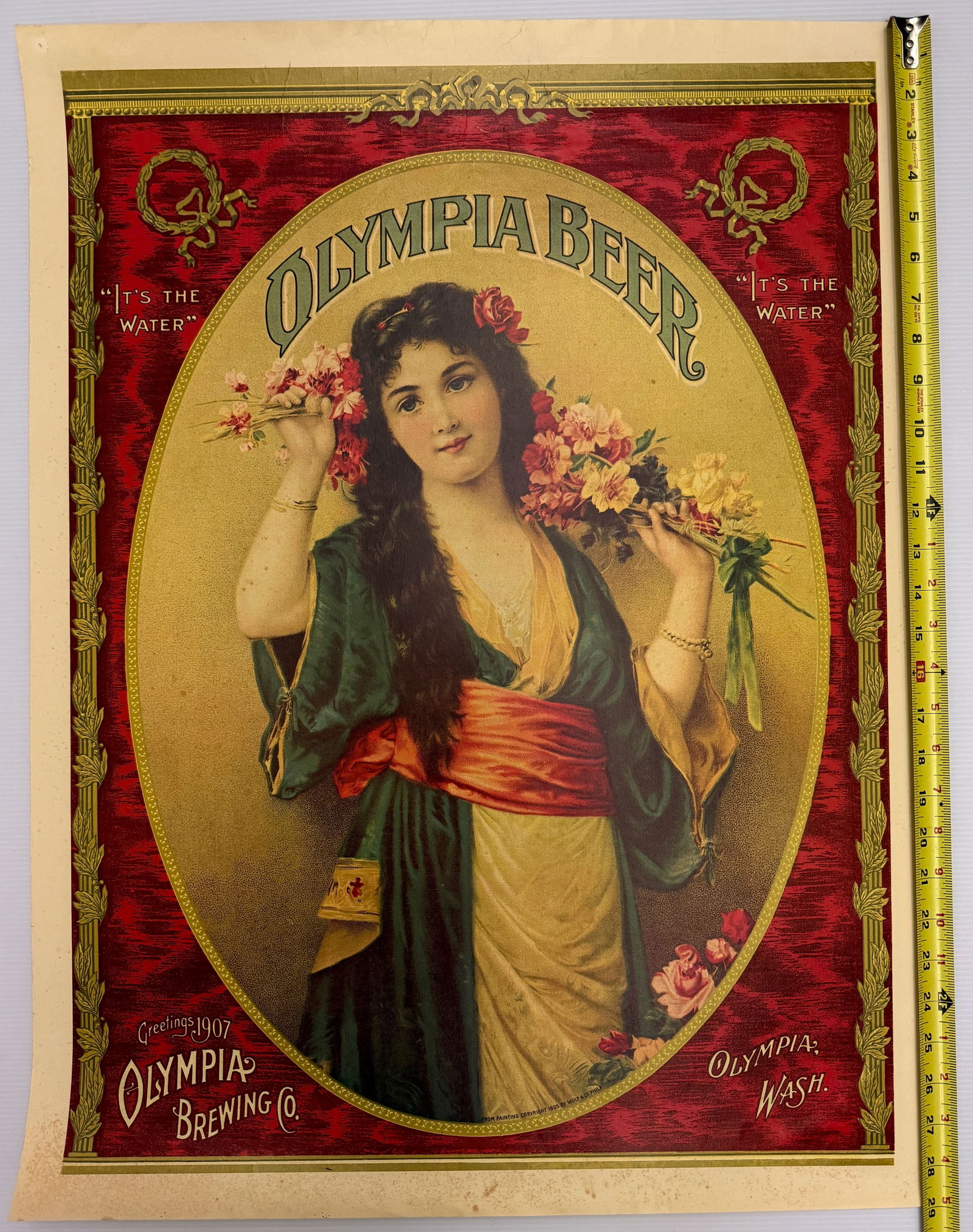 Olympia Beer brewing company: This item is a vintage advertising poster for the Olympia Beer brewing company, which operated in Tumwater, Washington. The poster features a Victorian-style woman holding flowers with the company's
