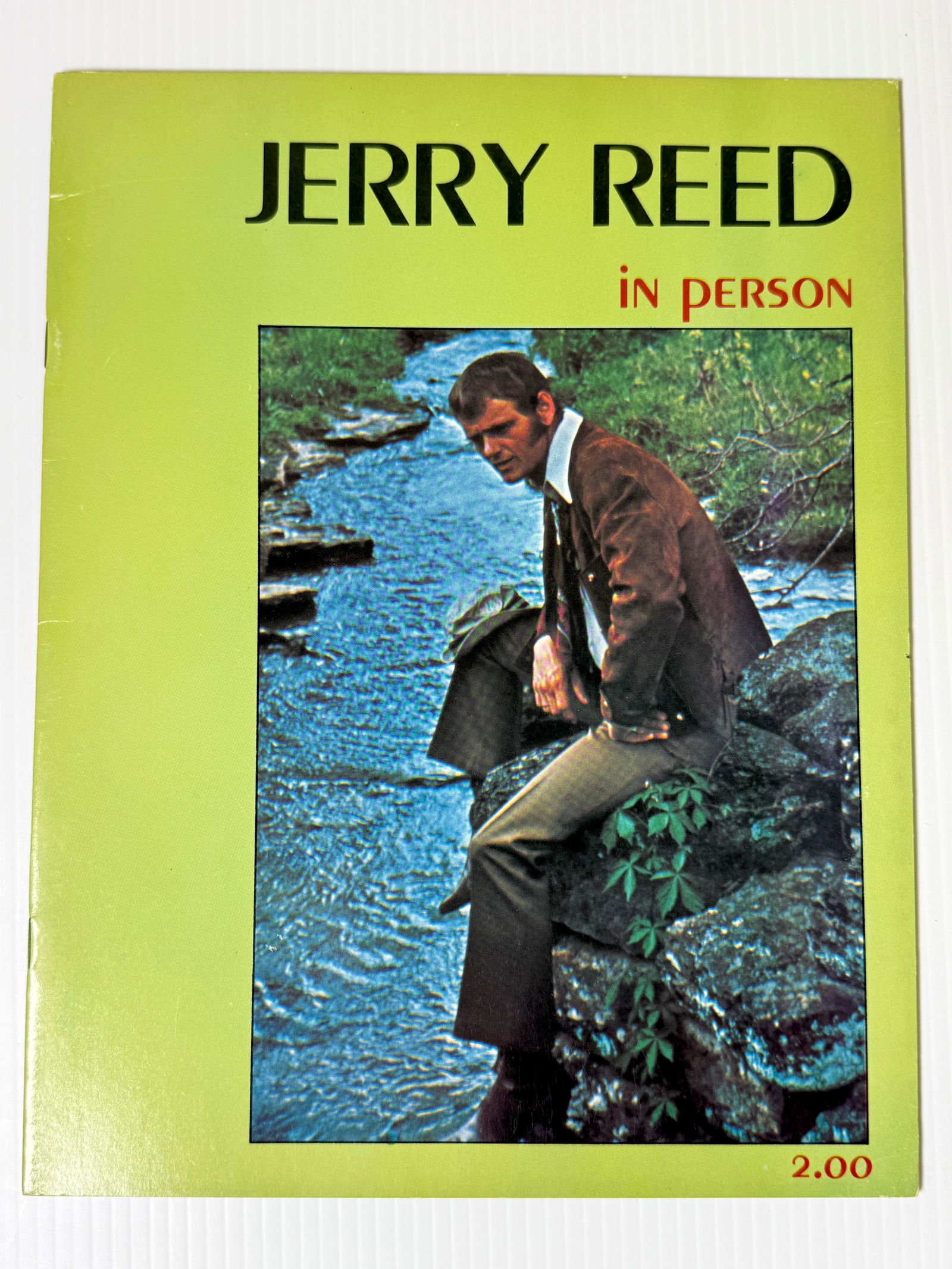 Concert program booklet Jerry Reed: concert program souvenir booklet for country musician and actor Jerry Reed. The cover features a photo of Reed sitting by a stream and indicates he is appearing "in person," with a price of $2.00. Jer