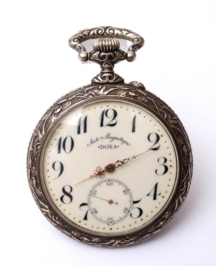 Jägeruhr, Doxa: Reliefiertes Gehäuse aus Silber(?). Auf der Rückseite reliefierte Darstellung zweier Jäger mit Hund. Weißes Zifferblatt mit arabischen Ziffern, Sekundenzifferblatt auf Sechs, durchbrochene Zeiger,