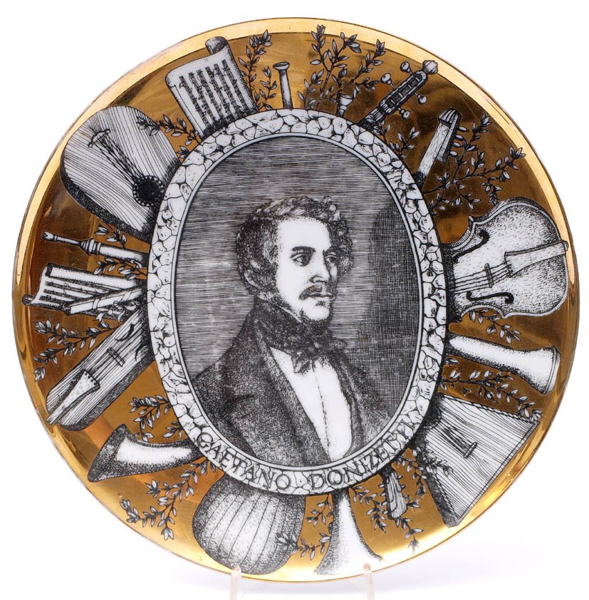 Wandteller, Piero Fornasetti, 60er Jahre: Flachgemuldete Form. Über Spiegel und Fahne Ovalmedaillon mit dem Portrait von Gaetano Donizetti, umgeben von zahlreichen Musikinstrumenten auf goldenem Fond. Schwarze Bodenmarke. Durchm.26cm.