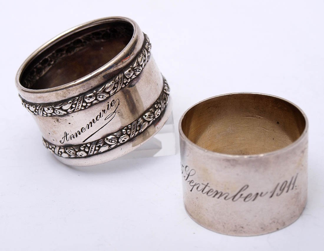Zwei Serviettenringe: Einer aus dem 19.Jhdt. mit gebundenen Fruchtgirlanden und der Inschrift 'Annemarie'; der andere glatt mit der Gravur '25. September 1911'. Unterschiedlich Durchmesser. Gew. zus. 27g.